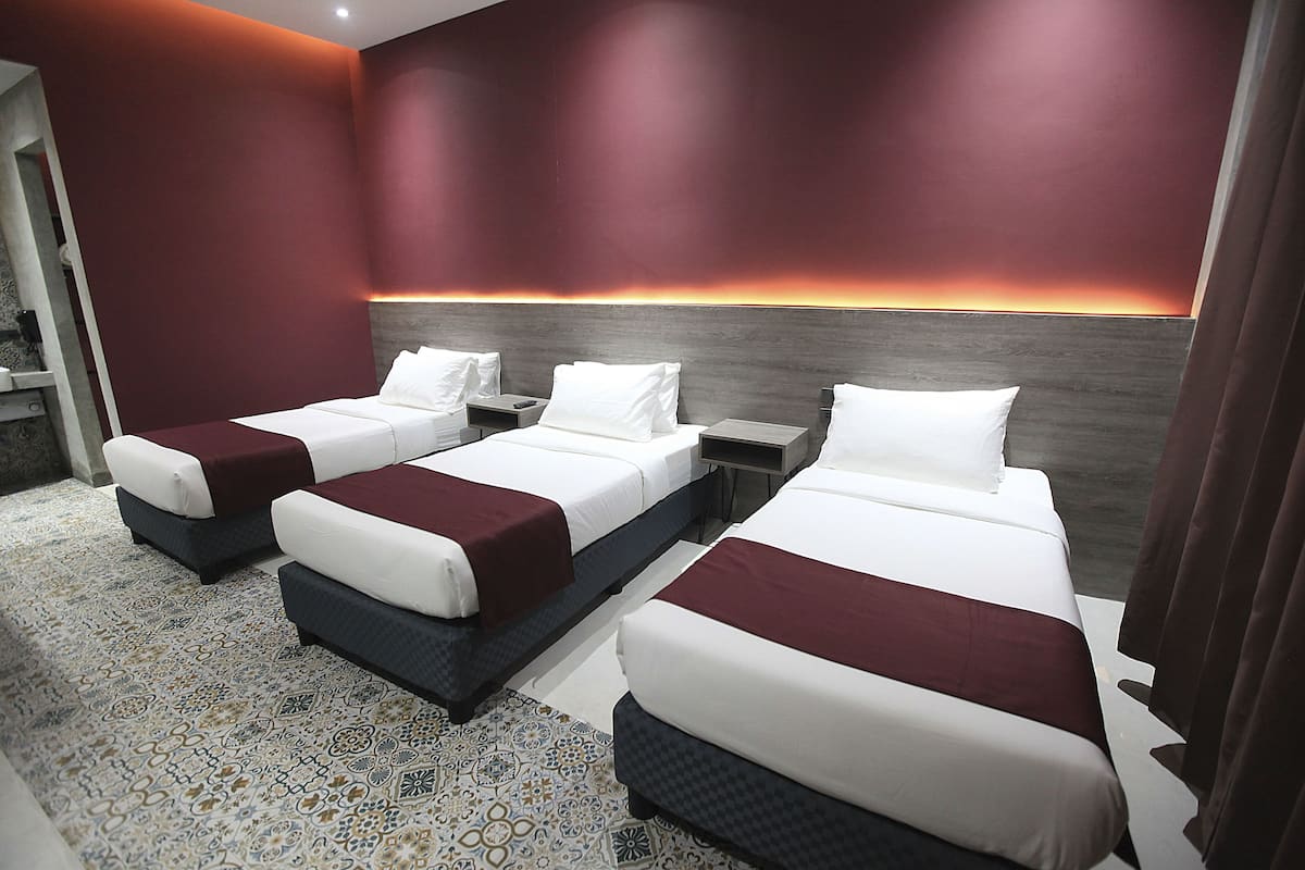 A hotel room with three beds, a patterned carpet, and a modern wall design.