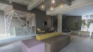 Un vestíbulo moderno con una amplia zona de estar, un aplique geométrico y un gran ventanal.