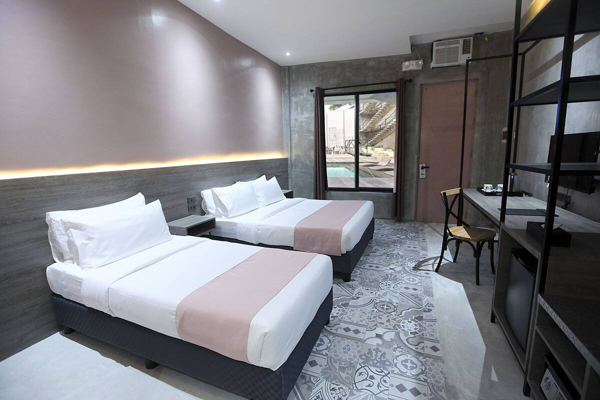 A hotel room with two beds, a desk, a chair, and a television.