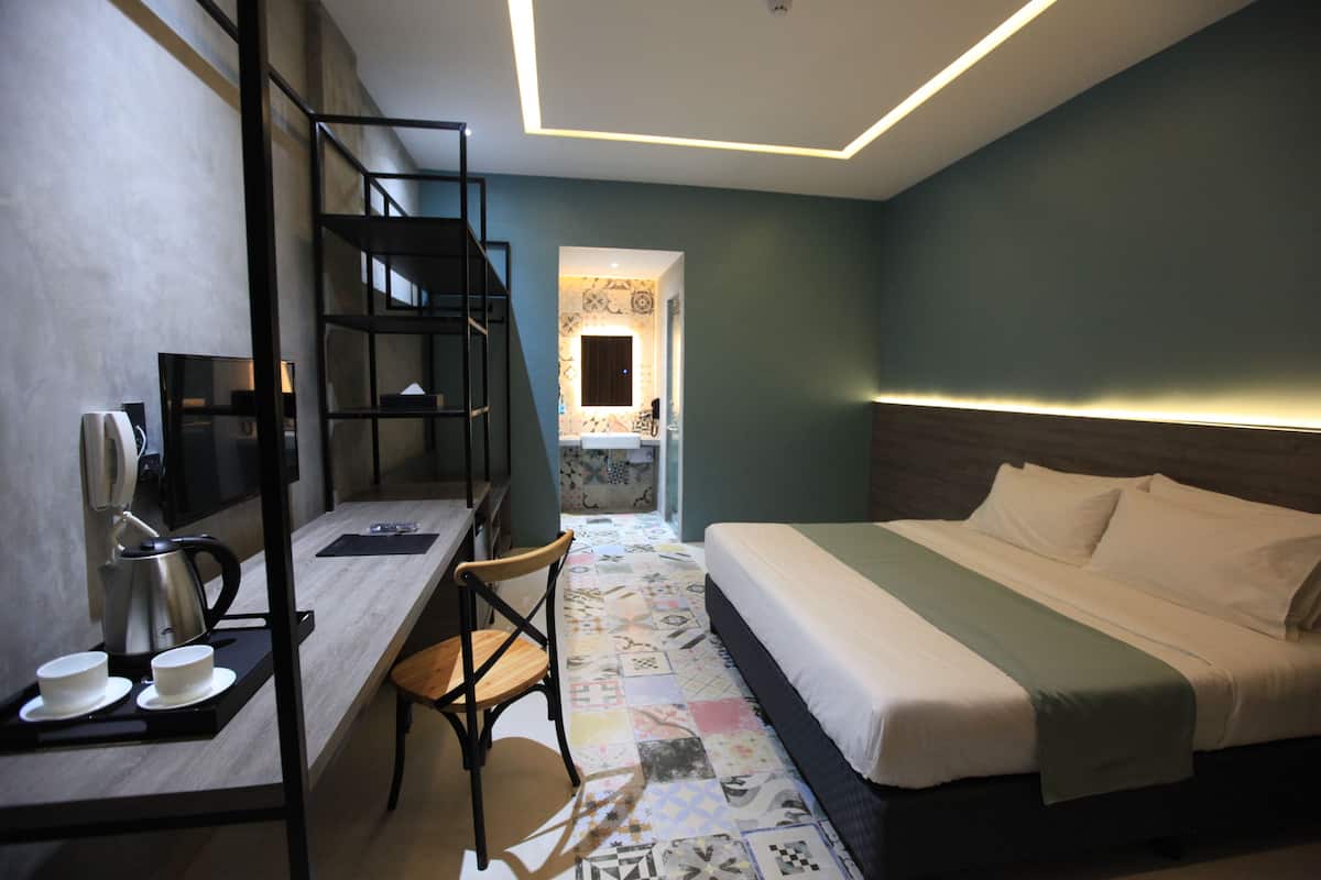 A hotel room with a bed, a desk with a chair, a coffee maker, and a shelf.