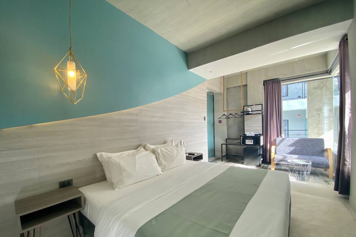 A modern hotel room with a large bed, a desk, and a seating area.