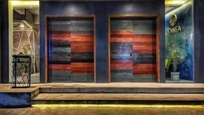 Entrada de hotel con dos puertas grandes, una escalera que sube y un letrero con la marca 'ZENVEA' a la derecha.
