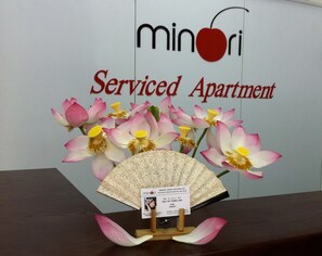 Schild für 'Minori Serviced Apartment' mit dekorativem Fächer und Blumen.
