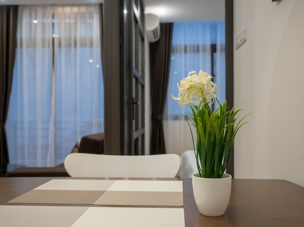Ein modernes Wohnzimmer mit Esstisch, einer Topfpflanze mit weißen Blüten und Blick ins Freie durch große Fenster.