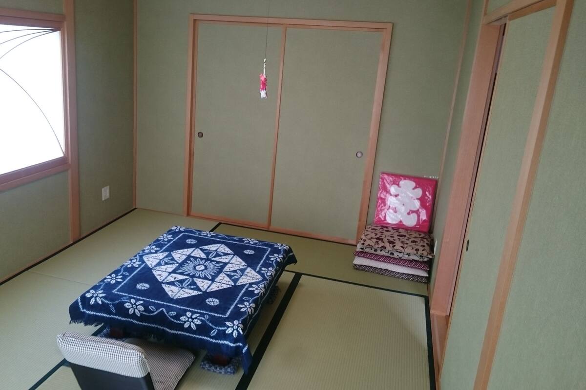 A traditional Japanese room with tatami flooring, a futon bed, a shoji screen door, and a small shelf with items.
