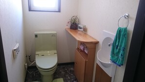 A small bathroom with a toilet, a wooden cabinet, a sink, and a window. - PittINN Farm Hinata (Kuroishi)