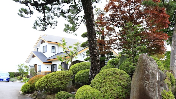A modern house with a white facade and grey roof, surrounded by well-maintained bushes and large rocks. - PittINN Farm Keyaki (Inakadate-mura)