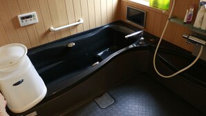 A bathroom with a bathtub, a handrail, a window, a shelf with toiletries, and a control panel. - PittINN Farm Keyaki (Inakadate-mura)