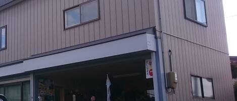 A two-story building with a garage door open, revealing a car inside. There is a sign with Japanese characters on the garage door.