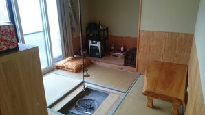 Une pièce avec un sol recouvert de tatamis, comprenant un futon, un radiateur, une radio et une petite étagère avec des bouteilles.