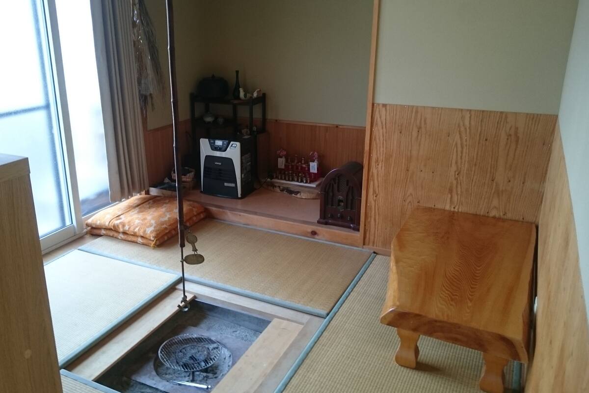 Una habitación con tatami, futón, calentador, radio y una estantería con botellas.