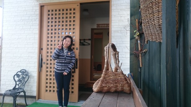 Une personne se tient devant un bâtiment doté d’une porte en bois et d’un panier tressé posé sur une table en bois.