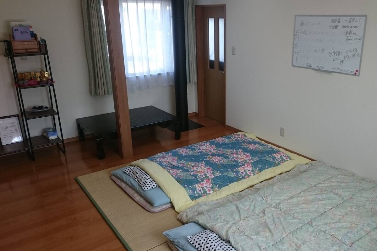 Un dormitorio con una cama, una estantería con objetos, un banco y una pizarra con escritura.