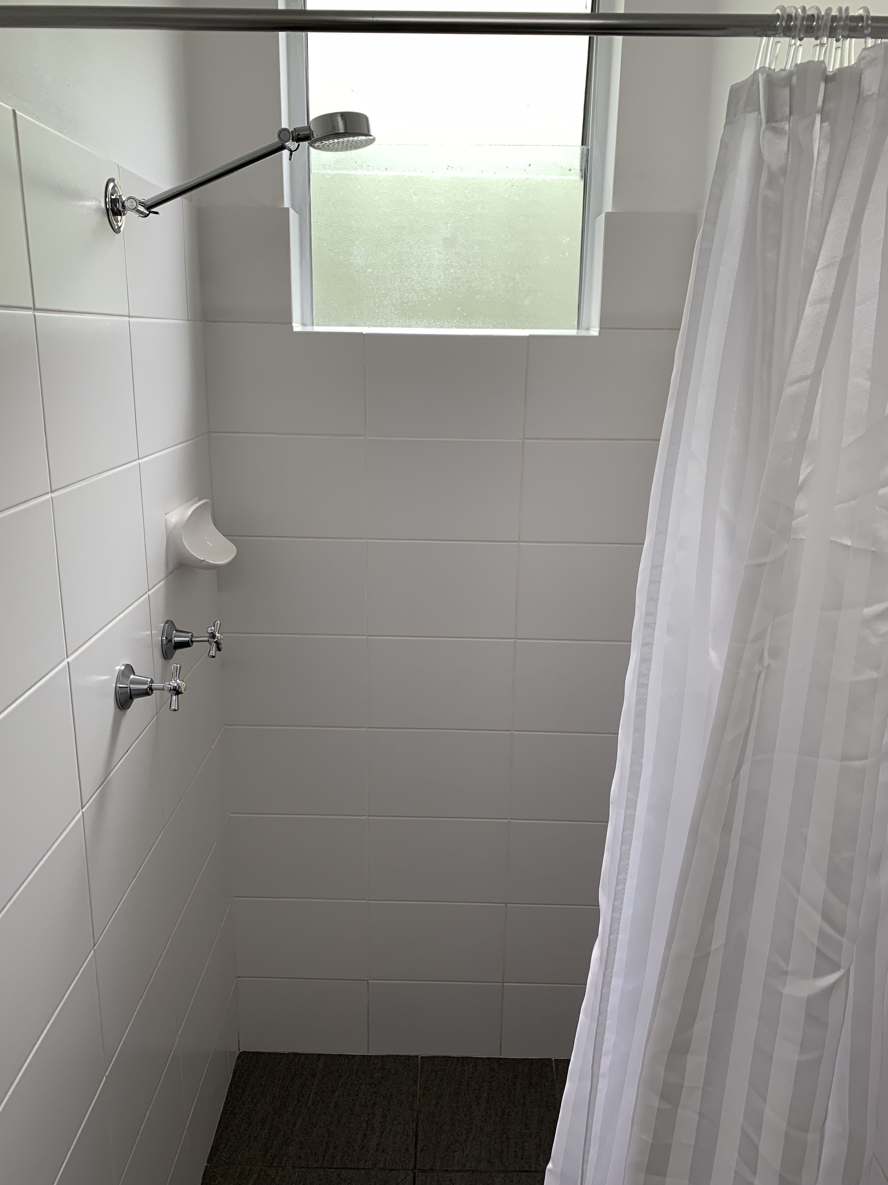 Een kleine betegelde badkamer met een douche, een raam en een toilet.