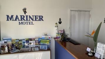 A reception desk at Mariner Motel with a white and blue color scheme, a lighthouse decoration, and various informational brochures and a calendar.