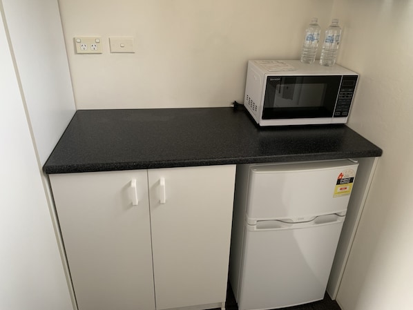 Una kitchenette con un microondas sobre una encimera negra, un refrigerador pequeño y dos botellas de agua.
