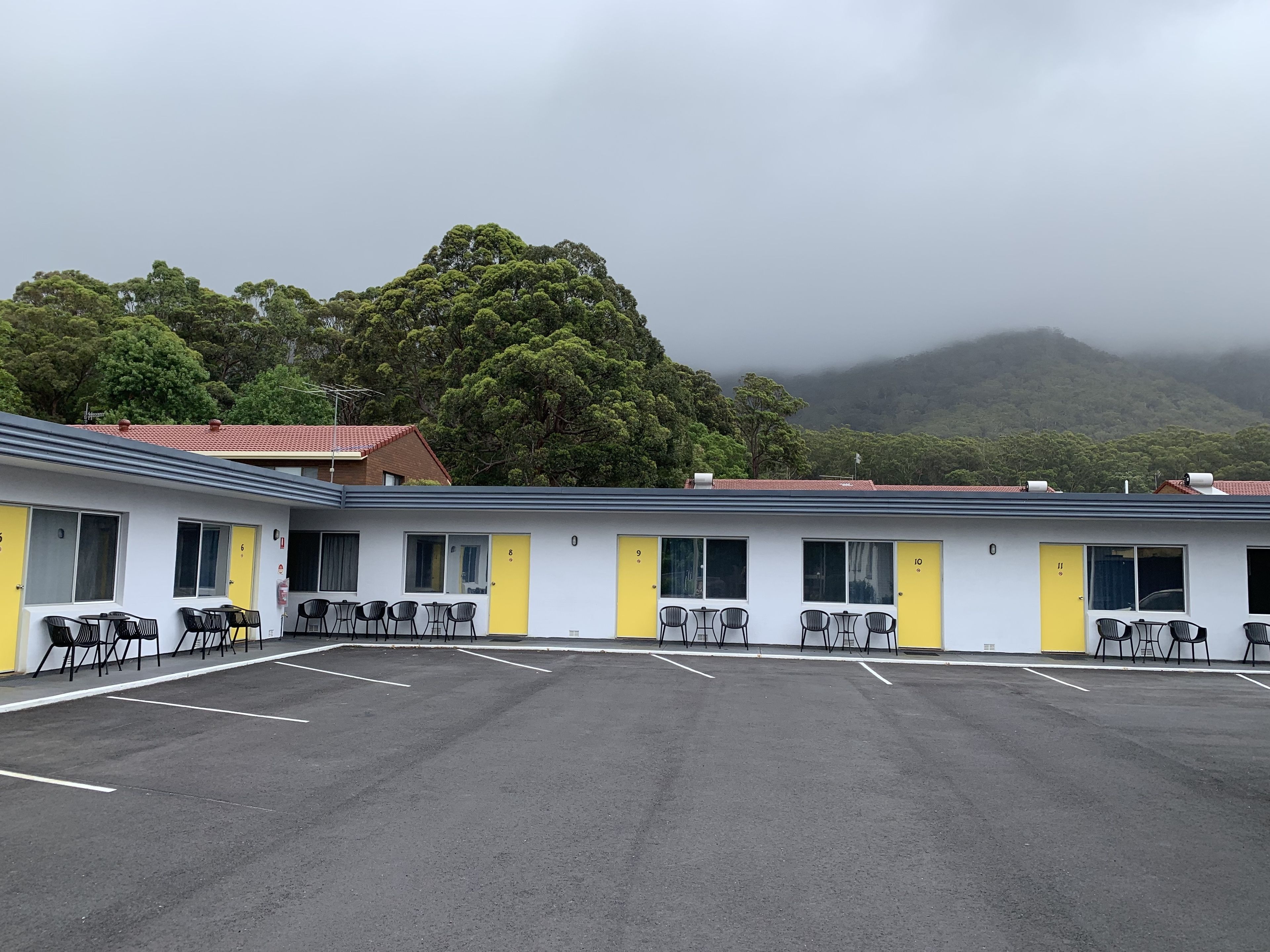 A motel with numbered rooms, outdoor seating, and a mountainous backdrop.