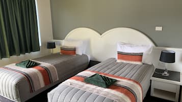 A hotel room with two beds, each with a striped bedspread and pillows, a nightstand with a lamp, and a window with green curtains.