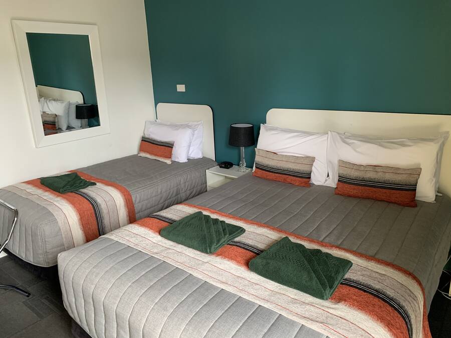 A twin bedroom with two beds, each with striped bedding and pillows, a nightstand with a lamp, and a mirror on the wall.