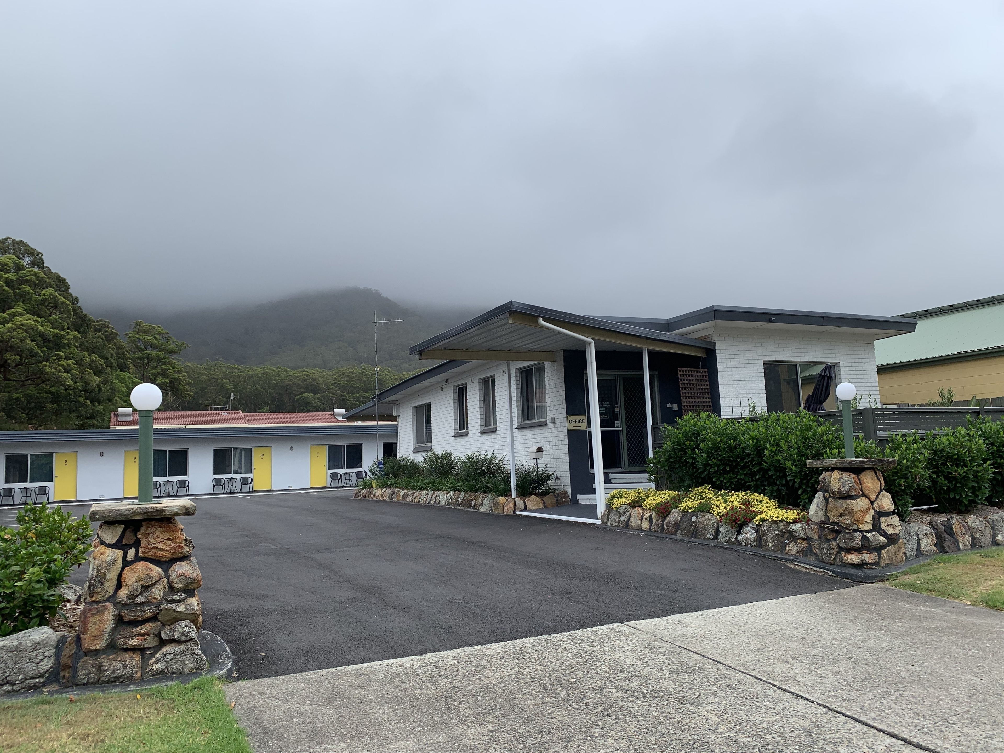 Un motel con un edificio de dos pisos, zona de estacionamiento techada y montañas al fondo.