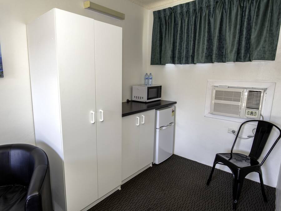 Ein kleines Zimmer mit einer Küchenzeile, einem schwarzen Stuhl, einem weißen Kleiderschrank und einem Fenster mit Vorhang.