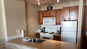 A compact kitchen with wooden cabinets, a microwave, a stove, and a refrigerator. - Cozy, ski-in/out, condo in the heart of Sun Peaks (Thompson-Nicola P)