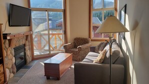 A cozy living room with a stone fireplace, a sofa, a coffee table, and a TV mounted on the wall. - Cozy, ski-in/out, condo in the heart of Sun Peaks (Thompson-Nicola P)