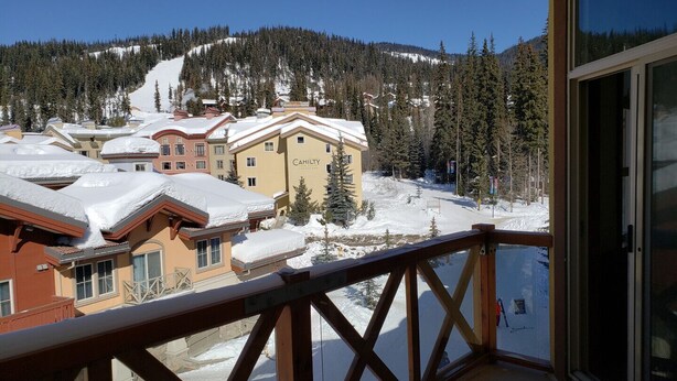 A snow-covered mountain resort with a view of a building labeled "CAHILTY" and a wooden balcony railing. - Cozy, ski-in/out, condo in the heart of Sun Peaks (Thompson-Nicola P)