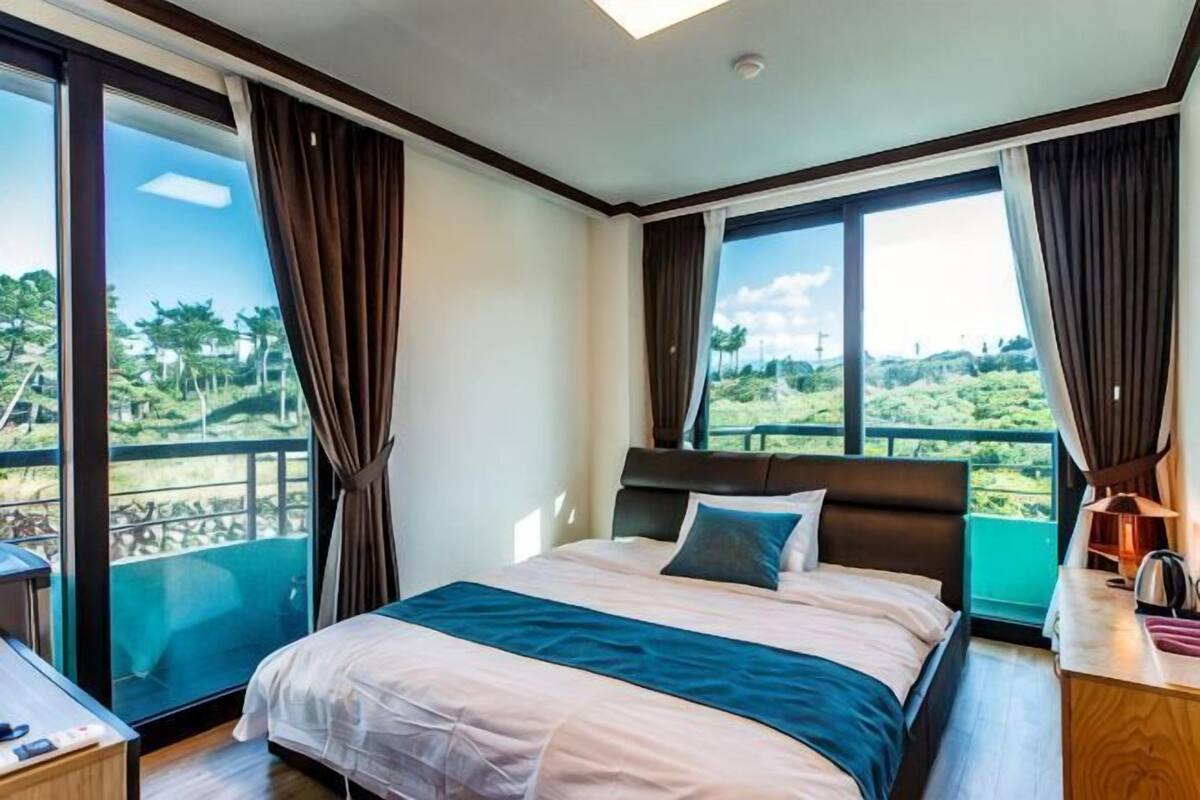 A bedroom with a large bed, a desk, and a view of a lush landscape.