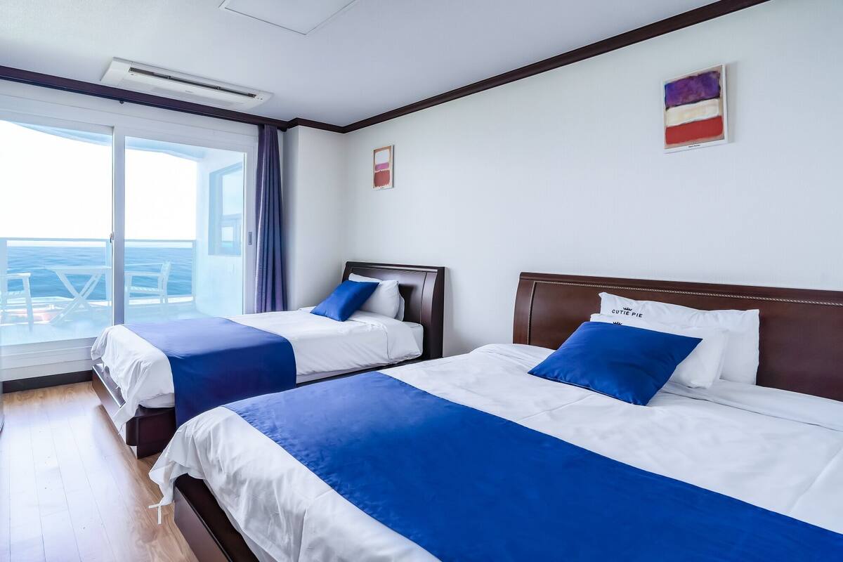 A hotel room with two beds, a large window with a view, and a ceiling fan.