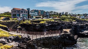 Uma área costeira com costa rochosa, uma ponte para pedestres e edifícios ao fundo.