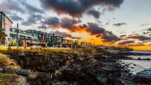 Um hotel costeiro com arquitetura moderna, litoral rochoso e vista para o pôr do sol.