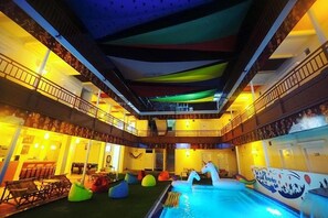 Un área de piscina interior con varios niveles, cortinas de techo coloridas, zonas de estar y un lounge junto a la piscina.