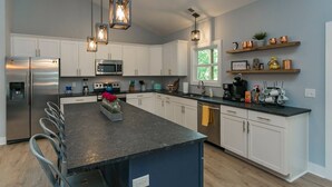 A modern kitchen with white cabinets, stainless steel appliances, and a central island with a vase of flowers. - BNA Blue Retreat, Game Room, Hot Tub (Nashville)