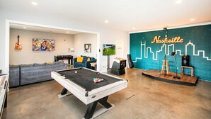A pool table in a room with a sofa, a guitar, and a wall with a city skyline mural. - BNA Blue Retreat, Game Room, Hot Tub (Nashville)