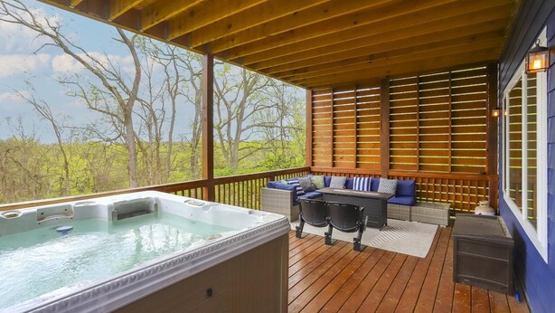 A wooden deck with a hot tub, outdoor seating, and a view of trees. - BNA Blue Retreat, Game Room, Hot Tub (Nashville)
