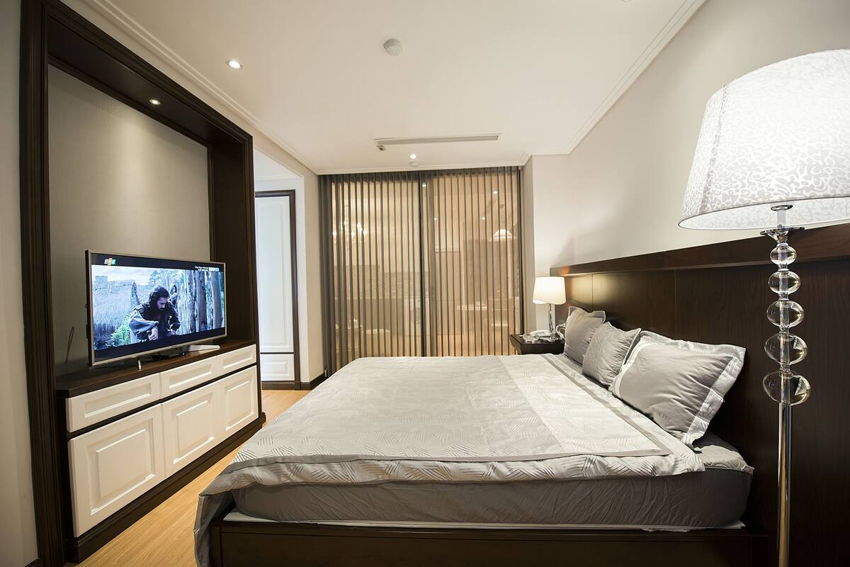 A modern hotel room with a large bed, a television on a cabinet, a bedside lamp, and a curtain.