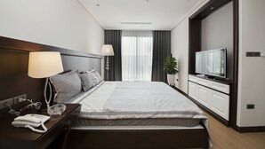 Una habitación de hotel moderna con una cama grande, una televisión, una mesita de noche con una lámpara y una planta.