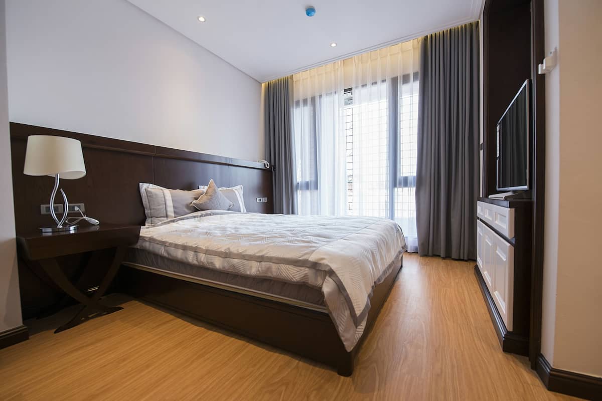 A hotel room with a large bed, a bedside table with a lamp, a TV, and a wardrobe.