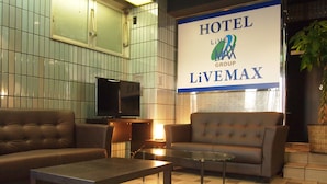 A hotel lobby with a large sign reading "HOTEL LIVEMAX GROUP". There is a television on a stand, a sofa, and a coffee table. - Hotel Livemax BUDGET Namba (Osaka)