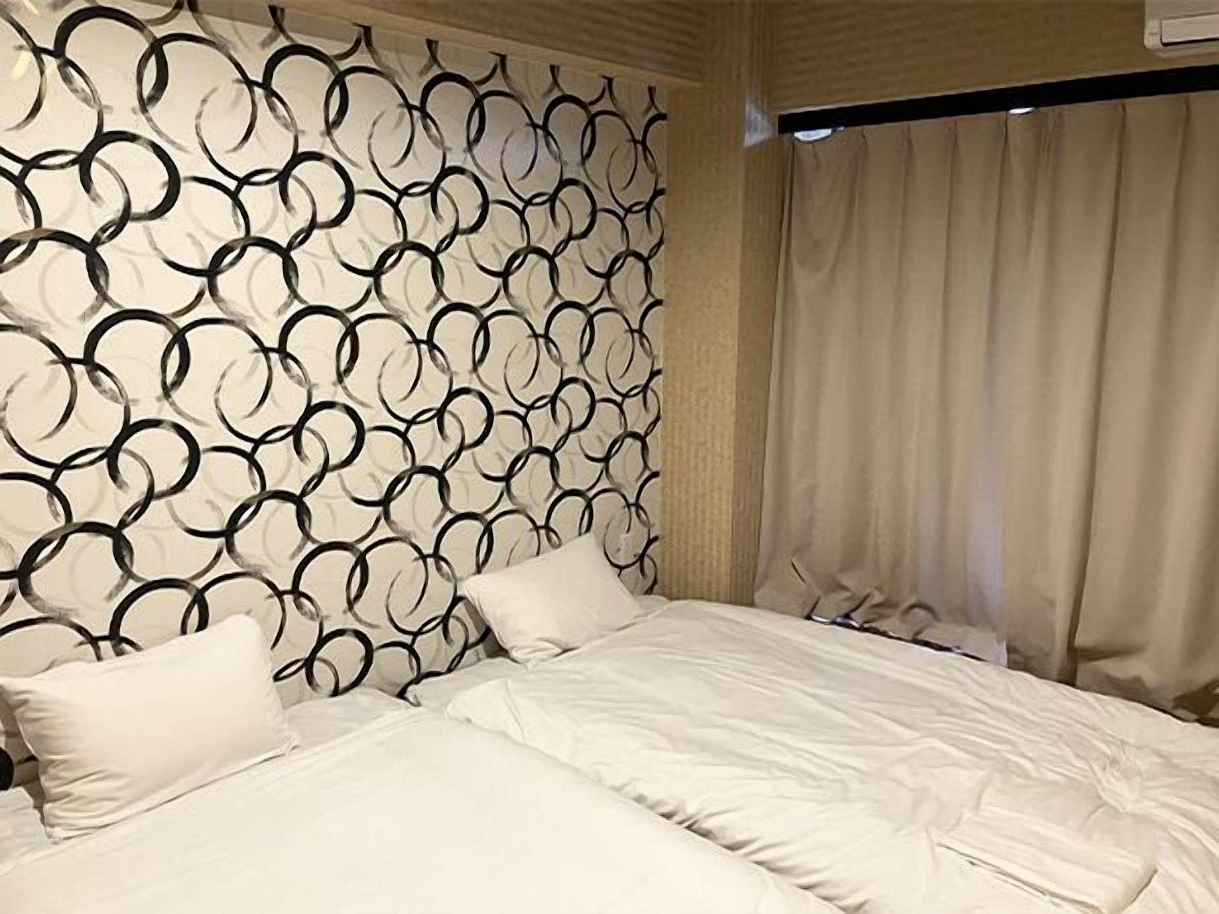 A hotel room with a patterned headboard, a bed with white bedding, and a window with curtains.