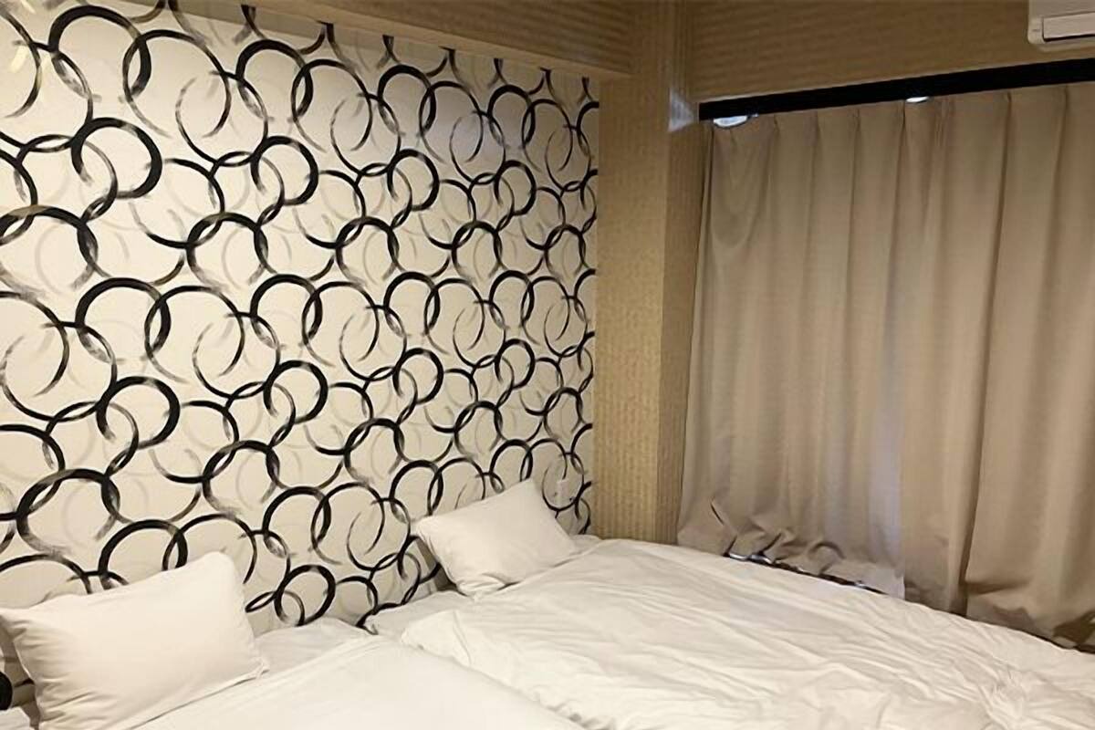 A hotel room with a patterned headboard, a bed with white bedding, and a window with curtains.