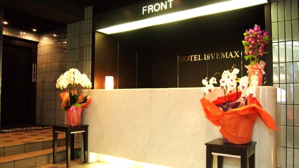 A hotel reception area with a 'FRONT' sign, a reception desk, and two flower arrangements. - Hotel Livemax BUDGET Namba (Osaka)