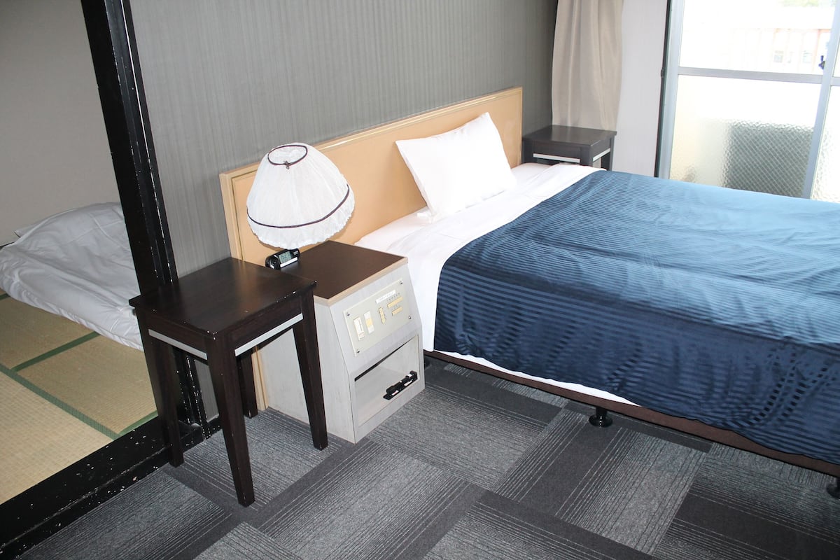 A hotel room with a bed, a nightstand, a lamp, and a dresser.