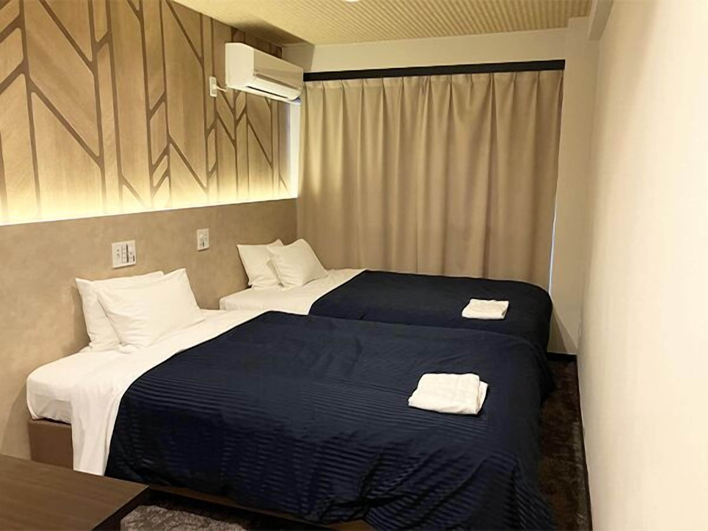 A hotel room with two beds, a wall-mounted air conditioner, and a curtain.
