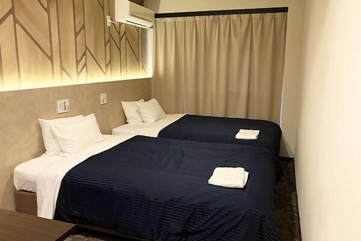 A hotel room with two beds, a wall-mounted air conditioner, and a curtain.