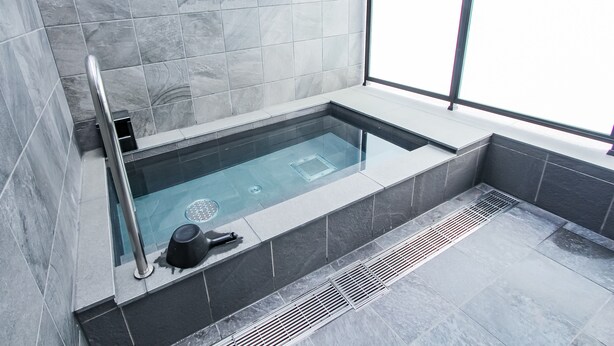 A modern bathroom with a glass-enclosed bathtub, grey tiles, and a window providing a view.