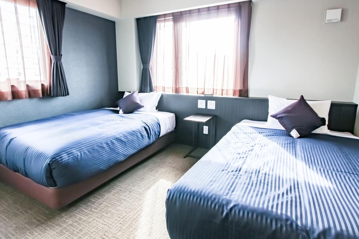 A hotel room with two beds, a small desk, and a window with curtains.