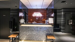 Un mostrador de recepción moderno con un reloj, una pantalla digital y una zona de espera con bancos.