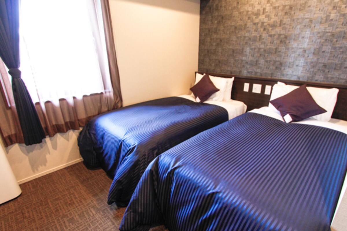 A hotel room with two beds, a brick-patterned wall, and a window with curtains.